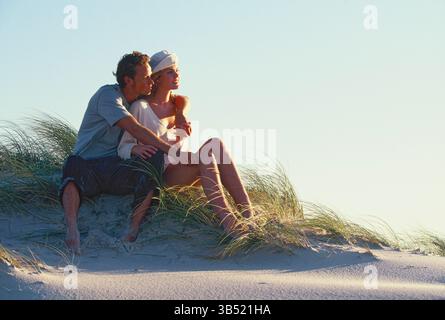 Giovane coppia romantica seduta su una duna di sabbia in spiaggia. Foto Stock