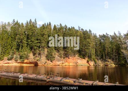Un paesaggio con una superficie d'acqua calma circondato da rocce rossastre ricoperte di alberi verdi, e soprattutto un cielo azzurro riflesso nel Foto Stock