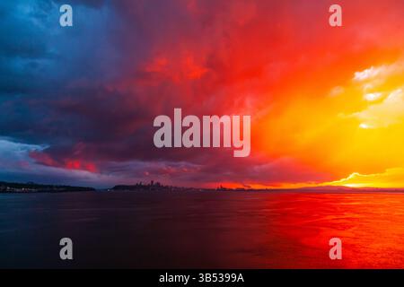 Colorato tramonto rosso e blu nella baia del mare al crepuscolo e la città in lontananza. Foto Stock