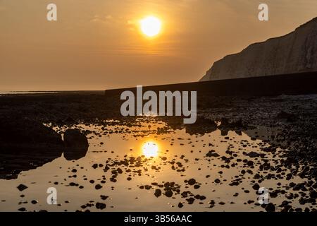 Il sole che tramonta e il suo riflesso nell'acqua con la bassa marea, al rifugio di pace nel Sussex Foto Stock