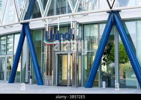 Milano, Italia - 8 aprile 2025: Sede Unipol a Milano. Moderno edificio esterno in vetro con colonne strutturali blu e logo Unipol sopra Foto Stock
