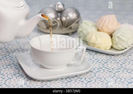Festa del tè. La padrona di casa versa il tè in tazze dal bollitore, in un pezzo di deliziosi marshmallows freschi, sul tavolo delle feste Foto Stock