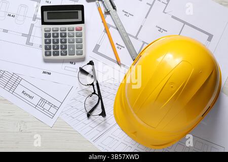 Diversi disegni architettonici, elmetto, matita, calibro a corsoio, calcolatrice e vetri su tavolo in legno chiaro, piatto Foto Stock