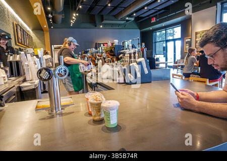 Davenport Florida, caffè Starbucks, bancone interno, barista lavoratrice che versa latte, uniforme con cuffia grembiule verde, area di preparazione del caffè, bevanda Foto Stock