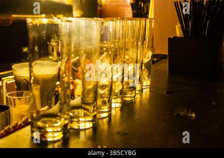 Una tazza di vetro piena di cubetti di ghiaccio collocati su un tavolo in un pub è un'immagine comune che rappresenta una bevanda fredda o un momento rinfrescante. Foto Stock