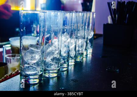 Una tazza di vetro piena di cubetti di ghiaccio collocati su un tavolo in un pub è un'immagine comune che rappresenta una bevanda fredda o un momento rinfrescante. Foto Stock