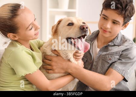 Sorella e fratello felici che abbracciano il carino cane Labrador a casa Foto Stock