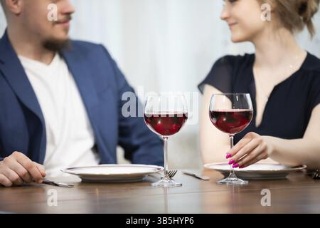 Un uomo e una donna si siedono a un tavolo. Entrambi sono elegantemente vestiti. Sul tavolo ci sono due piatti e due bicchieri di vino rosso. La donna sta tenendo in mano uno dei Foto Stock