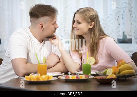Su un piedistallo da tavolo in legno con vari tipi di frutta. A tavola si siede una giovane coppia. L'uomo e la donna si stanno sorridendo l'un l'altro, e lei sta accarezzando Foto Stock