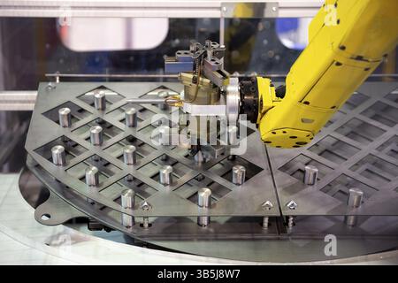 Il braccio robotico giallo dispone gli elementi metallici dopo la produzione. Apparecchiature automatiche per macchinari industriali Foto Stock