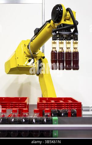 Il braccio robotizzato giallo dispone i flaconi di soda in plastica in una custodia di Ð°. Apparecchiature automatiche per macchinari industriali. Verticale Foto Stock