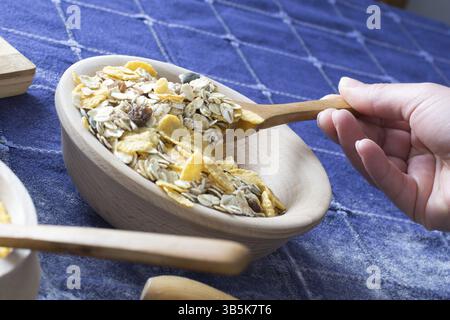 Femmina lato prelievo di cereali con il cucchiaio di legno dalla ciotola di legno sul tavolo di casa Foto Stock