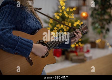 Un individuo che suona una chitarra nelle immediate vicinanze di un albero di Natale decorato splendidamente e festosamente Foto Stock