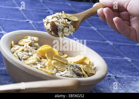 Femmina lato prelievo di cereali con il cucchiaio di legno dalla ciotola di legno sul tavolo di casa Foto Stock