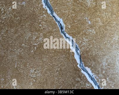 Primo piano di incrinature profonde della parete in una superficie di intonaco marrone ruvida. Struttura danneggiata, background astratto, assenza di persone, concetto di fragilità o riparazione. Foto Stock