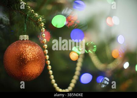 Un ornamento lucente a forma di palla di Natale rotonda attaccata a un albero di Natale su uno sfondo natalizio con luci in sughero Foto Stock