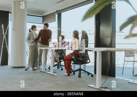 I colleghi si riuniscono in un ufficio luminoso e spazioso che migliora la collaborazione. Un incontro di idee fiorisce mentre un membro condivide le sue idee, circondato da foc Foto Stock
