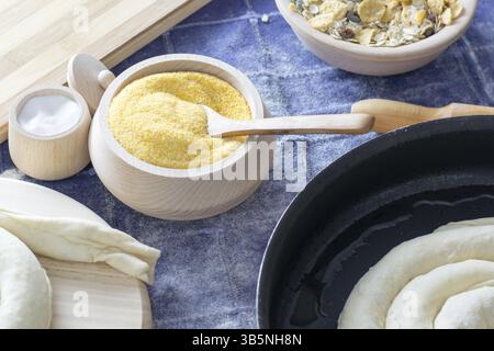Farina di mais nel recipiente di legno con un cucchiaio di legno. Farina di frumento visibile, farina di mais, cereali, piatto di legno Foto Stock