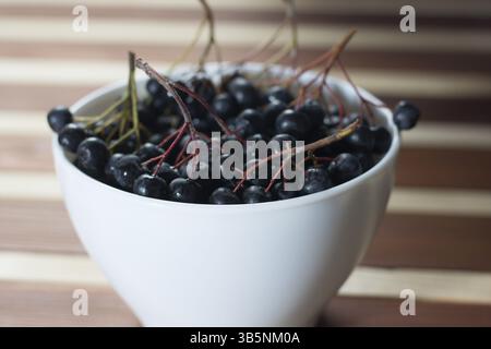 Primo piano della wet bacche di Aronia in bianco semplice ciotola sul tavolo di legno Foto Stock