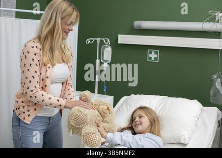 Una madre conforta il suo bambino malato in una stanza d'ospedale condividendo un prezioso orsacchiotto per un supporto emotivo Foto Stock