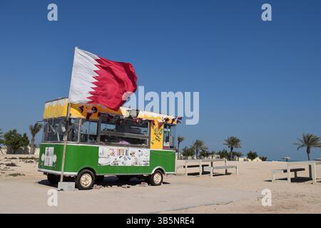 Vibrazioni costiere e orgoglio locale: Un colorato camion di cibo che sventola la bandiera del Qatar sotto il luminoso sole del deserto Foto Stock