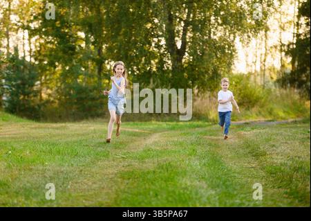 Ragazzo carino, ragazza che corre a piedi nudi sull'erba in estate in campagna. Fratello, sorella divertiti all'aperto a giocare a tag. Vacanze, attività ricreative di campagna, frien Foto Stock