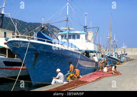 Barche da pesca nel porto di Portoferraio, Elba, Italia, nel 1975 - con i pescatori che riparano le reti alla banchina Foto Stock