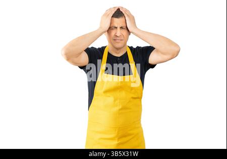 Venditore con grembiule giallo affetto da mal di testa disperato e stressato perché dolore e emicrania. Mani sulla testa isolate con sfondo bianco Foto Stock