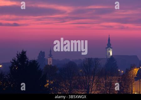 Tranquilla vista serale di un paesaggio urbano caratterizzato da torri e case della chiesa adagiate su un vibrante cielo al tramonto, evocando sentimenti di serenità e pace Foto Stock