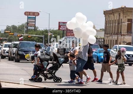 29 maggio 2022, Uvalde, Texas, Stati Uniti d'America: Una famiglia cammina attraverso l'autostrada 90 con palloncini e fiori sulla strada per Uvalde Town Square nel centro di Uvalde, Texas, il 29 maggio 2022. (Immagine di credito: © Josie Norris/San Antonio Express-News via ZUMA Press Wire) Foto Stock