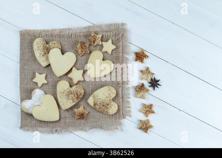 primi piani di biscotti a forma di cuore e stella su un sacco con biscotti a stella su sfondo bianco in legno. orizzontale Foto Stock