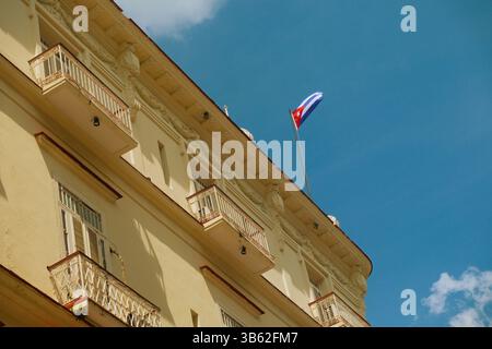 Bandiera cubana che sventola in cima a un edificio in stile coloniale con balconi nella vecchia Avana, Cuba, in una luminosa giornata di sole. Foto Stock