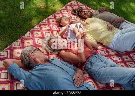 Una famiglia felice e multigenerazionale che si rilassa insieme sull'erba durante una giornata di sole, si diverte a divertirsi all'aperto. Foto Stock