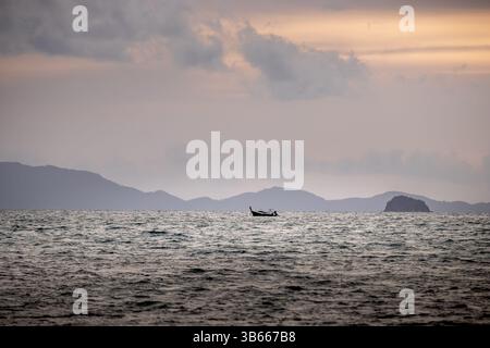 Questa immagine mostra una piccola barca al tramonto. La scena è dominata dalla vasta distesa dell'oceano, con dolci onde che si infrangono contro l'orizzonte Foto Stock