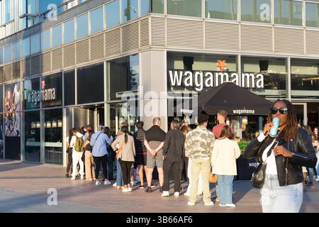 Una fila di clienti fa la fila lungo la strada fuori Wagamama a Londra, aspettando di essere accolti per un posto a sedere e un assaggio della cucina orientale, l'Inghilterra Foto Stock