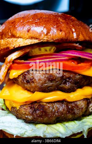 Un delizioso doppio cheeseburger con due polpettine di manzo, formaggio fuso, pancetta croccante e verdure fresche, che riposano su una foglia di lattuga. Perfe Foto Stock