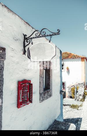 Insegna vuota del negozio vintage appesa a una staffa in ferro battuto ornato su una parete imbiancata ad Aldeia da Mata Pequena, perfetto spazio per il mockup di testo o. Foto Stock