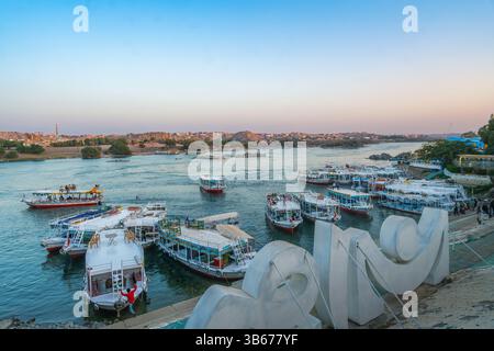 Diga di Assuan, Egitto - 15 gennaio 2025: Vista da un villaggio nubiano di barche turistiche attraccate al porto. Fiume Nilo e colline al crepuscolo con un cartello in primo piano Foto Stock