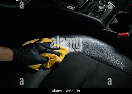 servizio di pulizia e dettaglio degli interni della vettura. uomo che pulisce sedili in pelle alcantara nera con detergente in schiuma e panno in microfibra Foto Stock