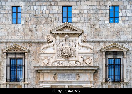 Una vista dettagliata della facciata di un edificio storico in pietra caratterizzato da elementi architettonici ornati, tra cui uno stemma, intagli decorativi e simmet Foto Stock