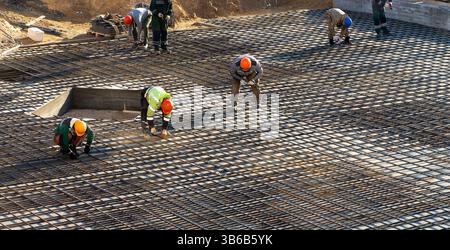 Brigata di costruttori di accessori per il versamento di calcestruzzo. Lavoratori che installano fili di legatura per rinforzare barre in acciaio nel cantiere Foto Stock