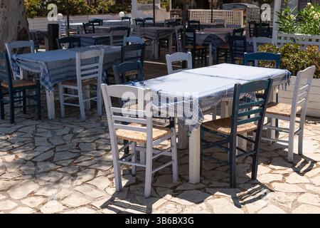 Tradizionale taverna greca all'aperto con tovaglie a scacchi blu e sedie in legno sotto la luce del sole. Foto Stock