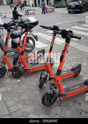 Cremona, Italia - 12 aprile 2025 noleggio di scooter elettrici arancione luminosi, un marciapiede acciottolato nei pressi di Piazza Stradivari sotto la Torr medievale Foto Stock