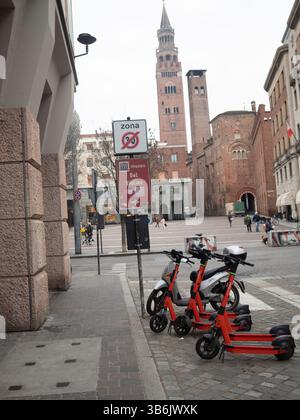 Cremona, Italia - 12 aprile 2025 noleggio di scooter elettrici arancione luminosi, un marciapiede acciottolato nei pressi di Piazza Stradivari sotto la Torr medievale Foto Stock