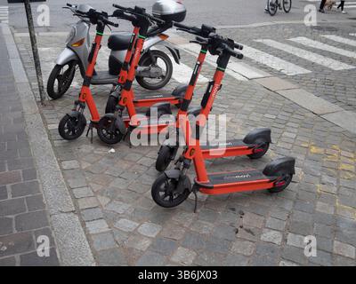 Cremona, Italia - 12 aprile 2025 noleggio di scooter elettrici arancione luminosi, un marciapiede acciottolato nei pressi di Piazza Stradivari sotto la Torr medievale Foto Stock