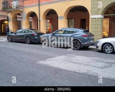 Cremona, Italia - 12 aprile 2025 Cupra Formentor e Tesla Model Y nere si trovano fianco a fianco sotto gli storici portici ocra su uno stretto ciottolo Foto Stock