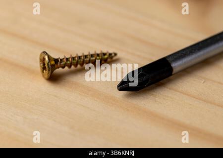 un cacciavite e viti autofilettanti decorative gialle per il fissaggio del legno su una tavola di pino, un gruppo di utensili per lavori di costruzione Foto Stock