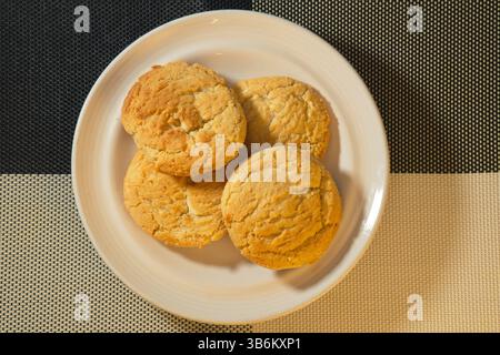 Biscotti alla macadamia al cioccolato bianco dorato su piatto bianco con sfondo testurizzato. Fotografia di prodotti da forno fatti in casa Foto Stock
