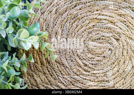 Primo piano di una trama circolare di paglia intrecciata con foglie verdi, creando uno sfondo naturale e rustico Foto Stock
