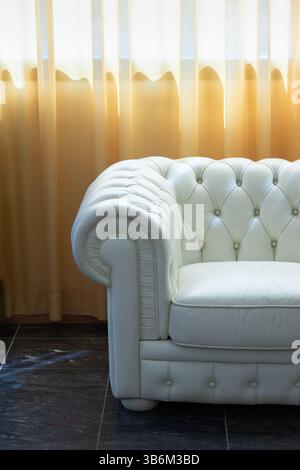 Divano chesterfield in pelle bianca in un hotel di lusso vicino a una finestra con eleganti tende gialle Foto Stock